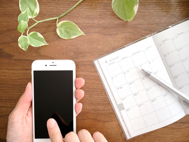 机上でスマホを操作する手とスケジュール帳